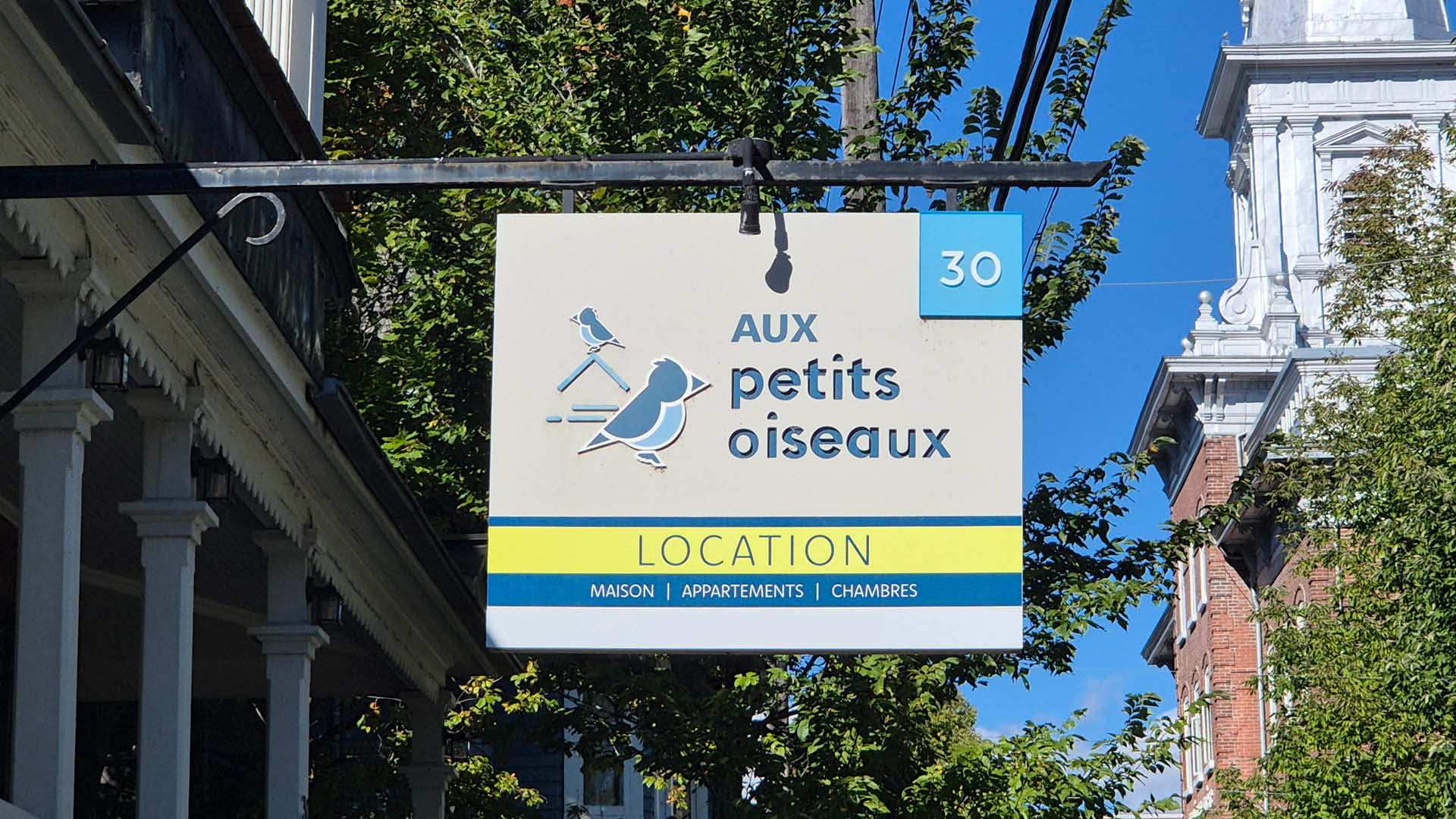 Das Schild des Hotels "Aux petits oiseux". Neben dem Schriftzug sind zwei Vögel abgebildet.